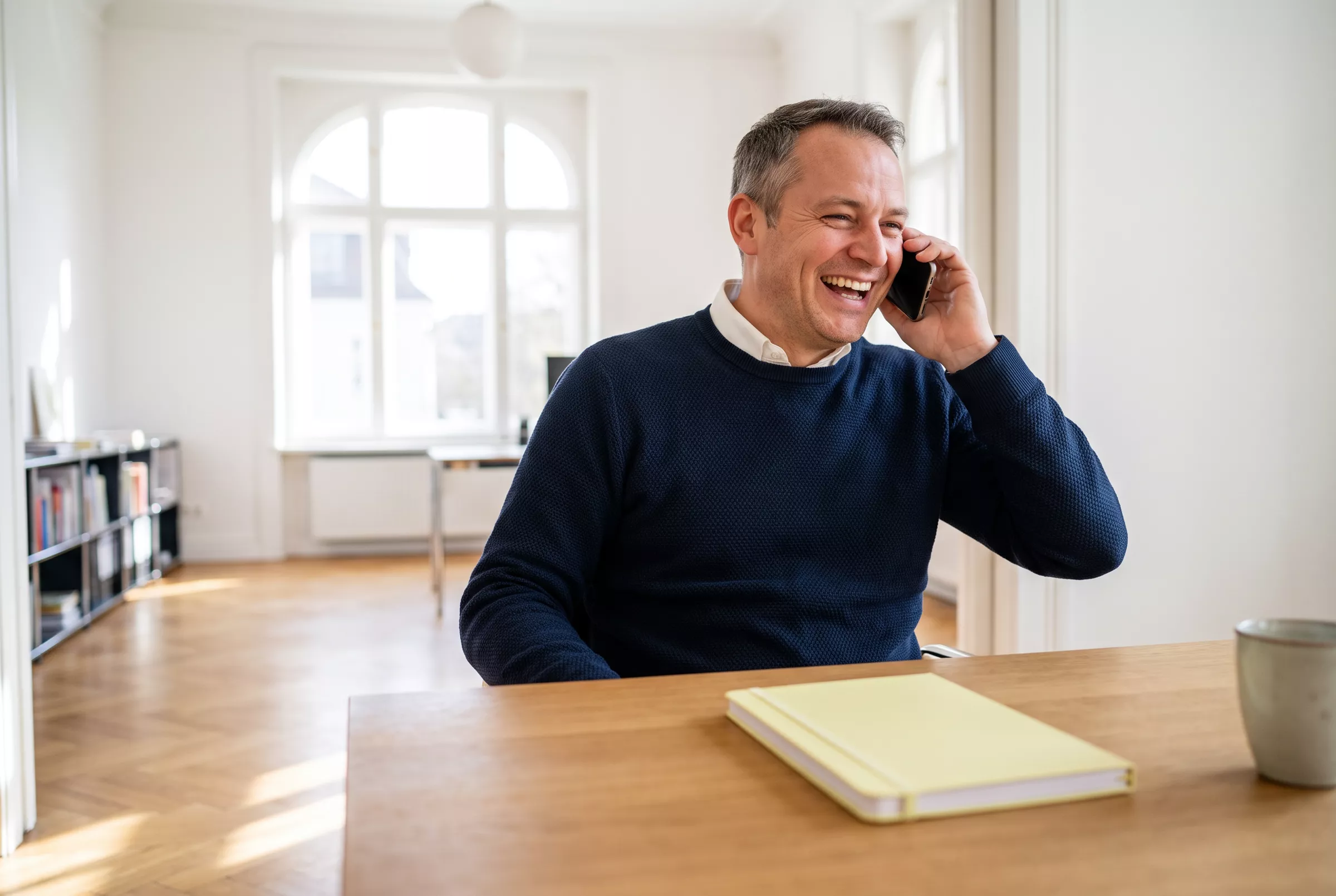 Makler lacht am Telefon in einem hellen Büro (KI-Bild)