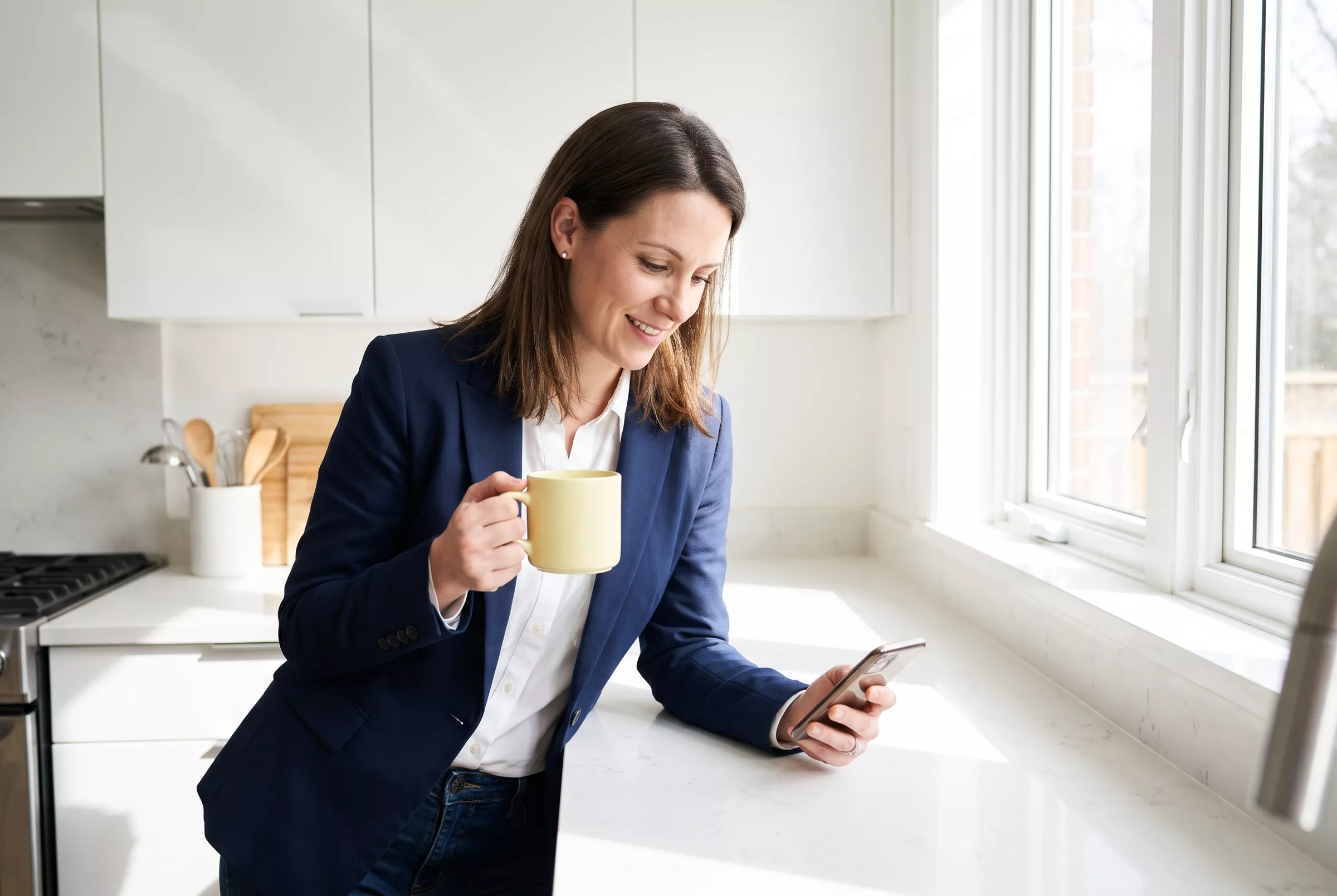 Maklerin mit Kaffeetasse liest morgens auf dem Handy (KI-Bild)